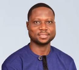 Professional corporate headshot of a Ghanaian male executive in a dark suit and light shirt, subtle smile, neutral light gray background, studio lighting, sharp focus